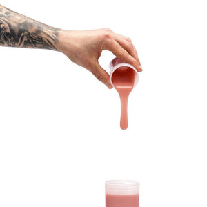 Hand pouring pink liquid from a small container onto a white background