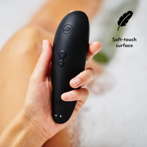 Black handheld Womanizer Classic 2 Massager with soft-touch surface held in a hand, on a blurred background.