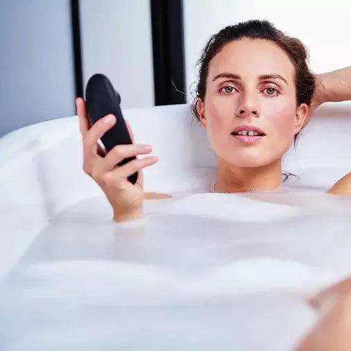 Woman in a bathtub with bubbles holding a black Womanizer Classic 2 Massager.